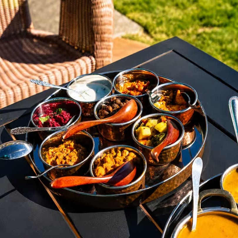 A thali platter with various Indian dishes in small copper bowls on an outdoor table.