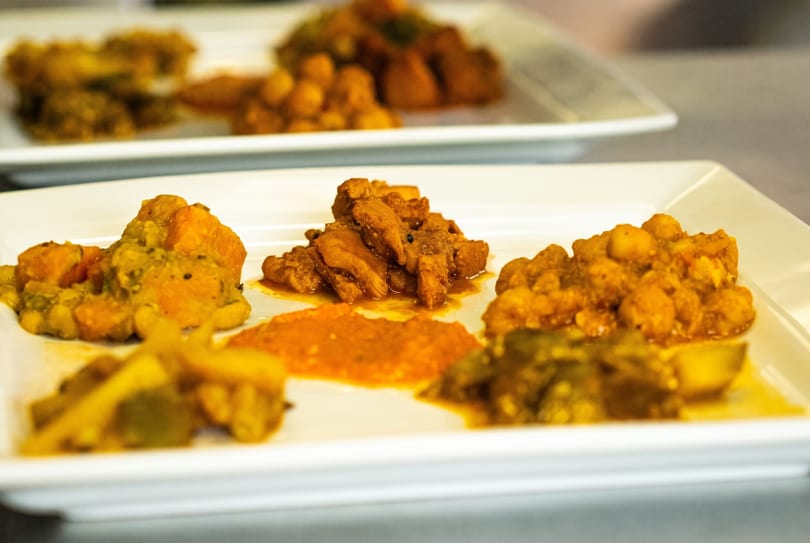 Two white rectangular plates filled with various portions of colorful Indian curries and chutneys.